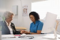Female doctor examining hand of senior patient in doctors office — Stock Photo