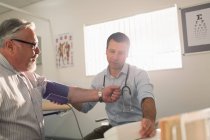 Чоловік-лікар, який перевіряє артеріальний тиск пацієнта у кабінеті огляду — стокове фото
