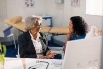 Female doctor talking with senior patient in doctors office — Stock Photo