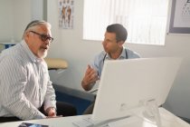 Male doctor meeting with senior patient at computer in doctors office — Stock Photo