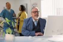 Médico varón que trabaja en la computadora en el consultorio médico - foto de stock