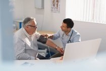Male doctor checking blood pressure of senior patient in doctors office — Stock Photo