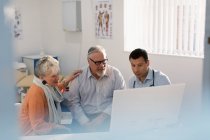 Встреча врача с пожилой парой за компьютером в кабинете врача — стоковое фото