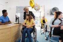 Женщина-регистратор приветствует пациентку в инвалидном кресле в клинике — стоковое фото