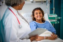 Усміхнена дівчина пацієнт розмовляє з лікарем в лікарняній кімнаті — стокове фото