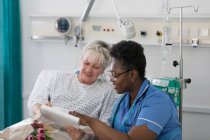 Жіноча медсестра обговорює документи з пацієнтом у лікарняній кімнаті — стокове фото