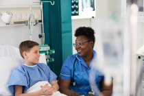 Жіноча медсестра розмовляє з пацієнтом-хлопчиком у лікарняній кімнаті — стокове фото