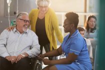 Female nurse talking with senior male patient in wheelchair in clinic lobby — Stock Photo