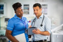 Médico varón con tableta digital hablando con enfermera en el hospital - foto de stock