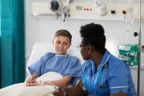 Enfermera hablando con niño paciente en habitación de hospital - foto de stock