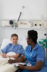 Enfermera con portapapeles hablando con niño paciente en habitación de hospital - foto de stock
