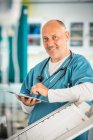 Retrato sonriente, confiado médico masculino usando tableta digital en el hospital - foto de stock