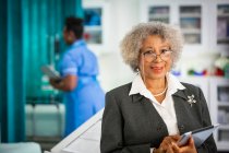 Portrait confident senior female doctor with digital tablet in hospital — Stock Photo