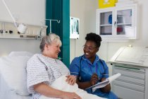 Enfermera hablando con paciente mayor en habitación de hospital - foto de stock