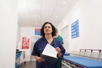Confident female doctor with medical chart making rounds in hospital corridor — Stock Photo