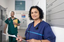 Portrait confident female doctor with medical chart, making rounds in hospital corridor — Stock Photo