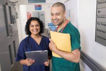 Portrait confident doctors with medical chart making rounds in hospital corridor — Stock Photo