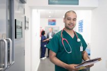 Retrato confiado médico varón con historial médico haciendo rondas en el pasillo del hospital - foto de stock