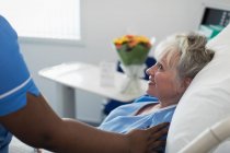 Enfermeira cuidadora reconfortante mulher idosa descansando na cama do hospital — Fotografia de Stock