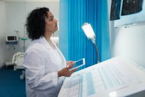 Зосереджена жінка-лікар з цифровим планшетом, що вивчає рентгенівські промені в лікарняній кімнаті — стокове фото