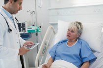 Arzt mit digitalem Tablet macht Runde, spricht mit Seniorin im Krankenhausbett — Stockfoto