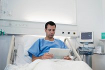 Paciente do sexo masculino em uso de comprimido digital, em repouso no leito hospitalar — Fotografia de Stock