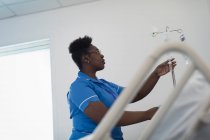 Женщина-медсестра регулирует капельницу внутривенно в больничной палате — стоковое фото