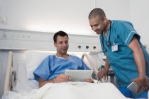 Männlicher Patient mit digitalem Tablet spricht mit Krankenschwester im Krankenhauszimmer — Stockfoto