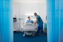 Медбрат разговаривает с пациентом, отдыхающим в палате больницы — стоковое фото