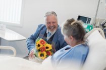 Щасливий старший чоловік з квітковим букетом, що відвідує дружину в лікарні — стокове фото