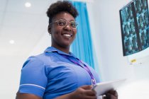 Retrato enfermeira confiante com tablet digital examinando raios-x no quarto do hospital — Fotografia de Stock