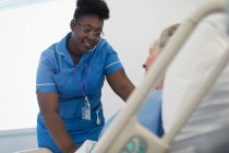 Усміхнена, дбайлива жінка медсестра розмовляє з пацієнтом у лікарняному ліжку — стокове фото
