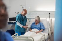 Médecin avec tablette numérique faisant des rondes, parler avec le patient âgé dans la chambre d'hôpital — Photo de stock