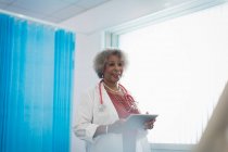 Старший жіночий лікар з цифровим планшетом робить набої в лікарняній кімнаті — стокове фото