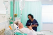 Arzt spricht mit Patient hinter IV-Tropf im Krankenhauszimmer — Stockfoto