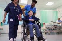 Medico e infermiera spingendo paziente ragazzo in sedia a rotelle nel reparto ospedaliero — Foto stock