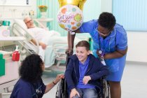 Médico e enfermeiro conversando com menino paciente em cadeira de rodas na enfermaria do hospital — Fotografia de Stock