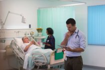 Médecin masculin avec tablette numérique faisant des rondes dans la chambre d'hôpital — Photo de stock