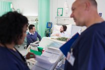 Ärzte mit medizinischem Diagramm machen Runde, im Hintergrund ruht der Patient im Krankenhausbett — Stockfoto