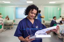 Medico donna concentrato che fa il giro, guardando la cartella clinica nel reparto ospedaliero — Foto stock