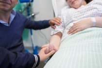 Любий син тримає руки з матір'ю, що відпочиває в лікарняному ліжку — стокове фото