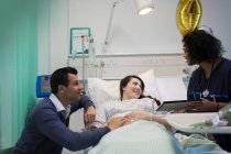 Médecin avec tablette numérique faisant des rondes, parler avec couple dans la chambre d'hôpital — Photo de stock