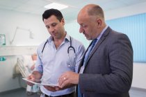 Чоловіки-лікарі з цифровим планшетом роблять раунди, консультування в лікарняній кімнаті — стокове фото