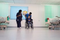 Medico e infermiera spingendo paziente ragazzo in sedia a rotelle nel reparto ospedaliero — Foto stock