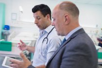 Médicos masculinos con tableta digital haciendo rondas, consultoría en habitación de hospital - foto de stock