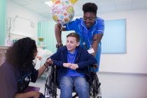 Arzt und Krankenschwester schieben Jungen im Rollstuhl auf Krankenhausstation — Stockfoto