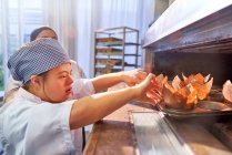 Junge Frau mit Down-Syndrom stellt Muffins in den Ofen — Stockfoto