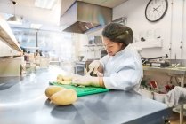 Молодая женщина с синдромом Дауна режет картошку на кухне кафе — стоковое фото