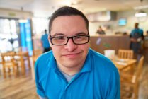 Close up portrait smiling young man with Down Syndrome in cafe — Stock Photo