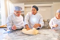 Instructor teaching students with Down Syndrome how to roll dough — Stock Photo